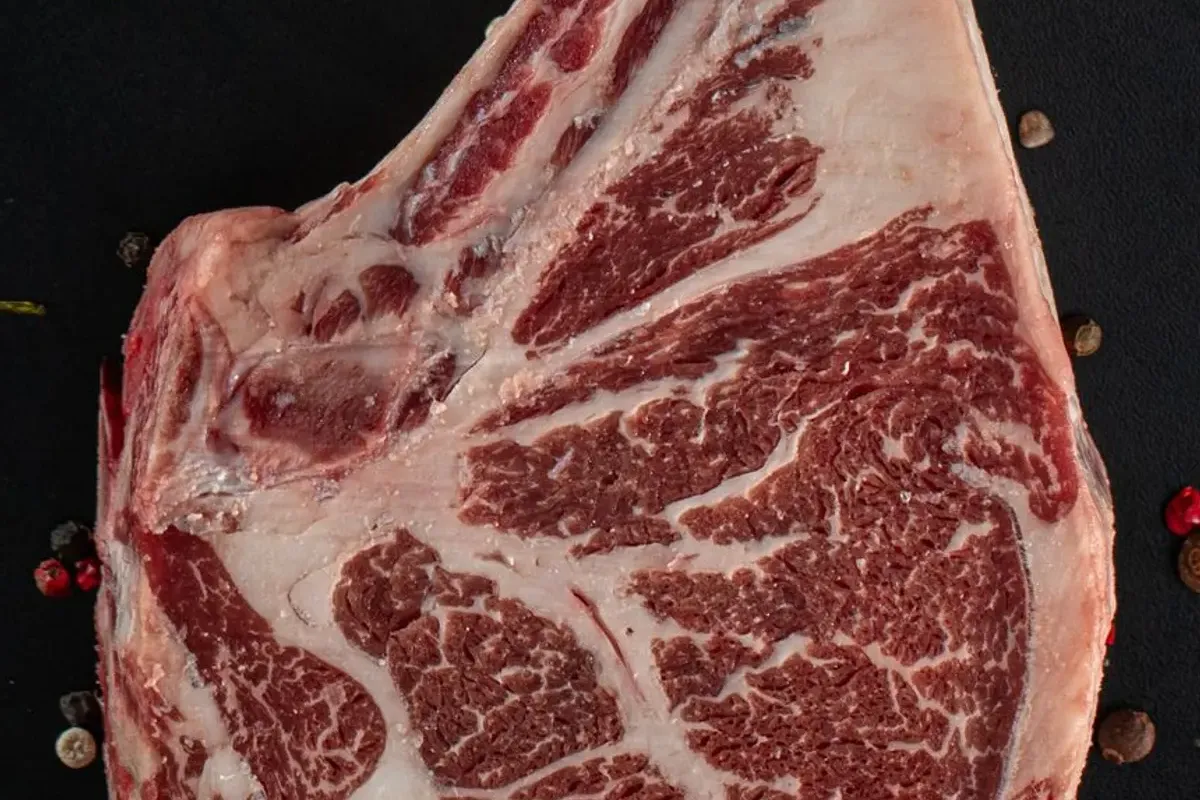 Raw bone-in rib steak on a dark surface